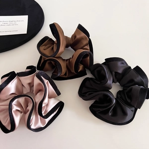 Detailed view of three satin scrunchies with black velvet edges in champagne, brown and black