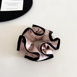 Close-up of pink satin scrunchie with black velvet trim and rich elegant pleats