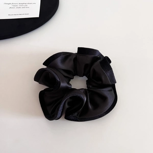 Detailed view of black satin scrunchie with velvet trim on minimalist white background