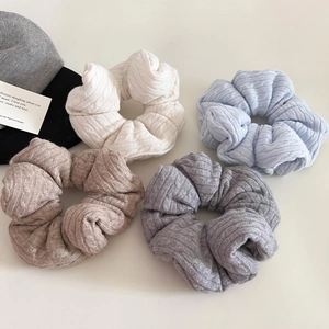 Detailed cable knit texture of four scrunchies in cream, blue, camel, and grey colors