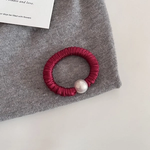 Détail d'un chouchou en satin rouge orné d'une grande perle blanche sur fond texturé gris