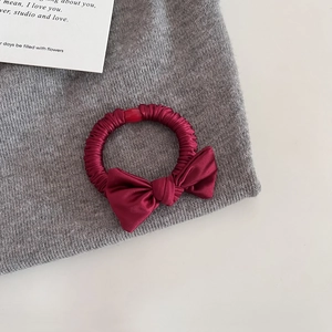 Détail d'un chouchou en satin bordeaux avec nœud sur un fond en tricot gris doux