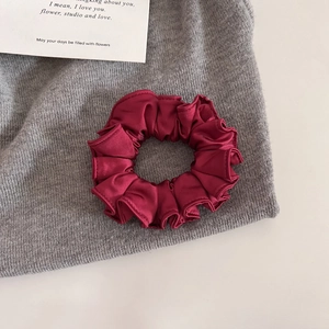 Gros plan sur chouchou en satin bordeaux avec texture plissée élégante sur tissu gris