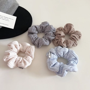 Detail showing knit scrunchies with cable pattern and fabric labels in soft pastel colors