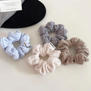 Close-up of four cable-knit hair scrunchies in blue, grey, cream, and brown colors
