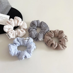 Close-up of four knitted cable-knit hair scrunchies in assorted soft winter colors
