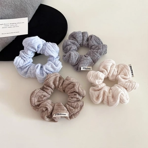 Close-up of four knitted scrunchies with ribbed texture and woven brand labels
