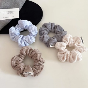 Detail of four cable-knit scrunchies in blue, grey, beige and brown with woven labels