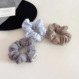 Three knitted scrunchies in blue, brown, and grey with a stylish ribbed texture design