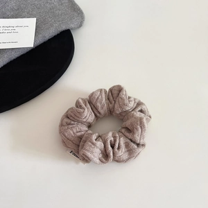 Detailed macro view of taupe knitted scrunchie showing fine ribbed texture and white label