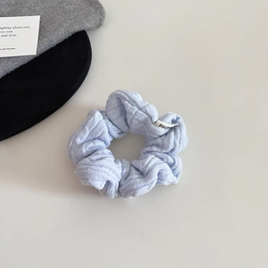Detailed view of a light blue knitted scrunchie with soft texture and white brand label