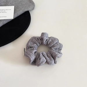 Detail of grey knitted scrunchie with brand label on a textured aesthetic background