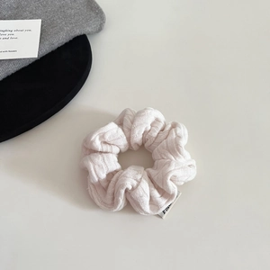 Detail shot of a cream knit scrunchie featuring chunky cable knit texture and brand label