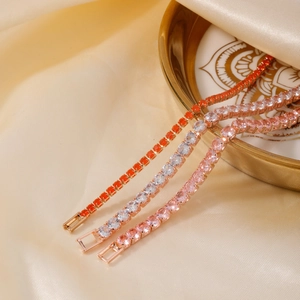 Drie zirkoon tennisarmbanden in oranje, wit en roze op gouden stoffen achtergrond
