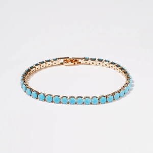Luxurious gold-plated tennis bracelet with round turquoise-colored stones on white background