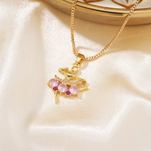 Collana con ciondolo ballerina dorata e zirconi rosa su morbido sfondo di seta beige