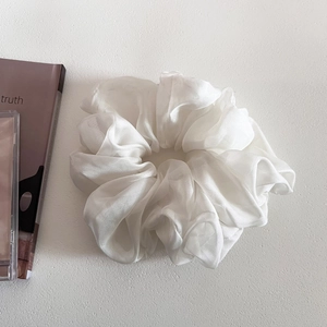 Close-up of a large white mesh scrunchie with soft fabric pleats on a gray surface