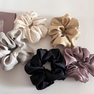 Flat lay of five glossy satin scrunchies in cream, gold, silver, black, and pink colors