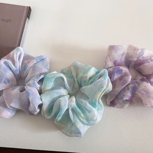 Detail of three tie-dye chiffon scrunchies in pastel blue, green and purple watercolor patterns