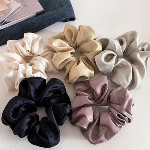 Close-up of five glossy satin scrunchies in cream, champagne, silver, black, and dusty pink