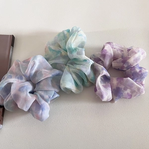 Detailed view of three chiffon tie-dye scrunchies in pastel pink, blue, and green tones