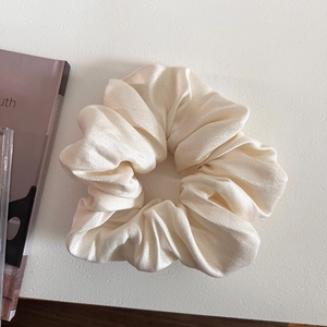 Close-up of a large cream-colored satin scrunchie with a soft silk texture and elegant folds