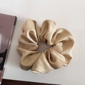 Detailed close-up of champagne gold satin scrunchie showing glossy texture and rich pleats