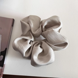 Macro detail of champagne gold satin scrunchie with soft silk texture and elegant pleats