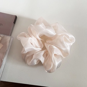 Close-up of champagne pleated organza scrunchie with a soft pearlescent glossy texture
