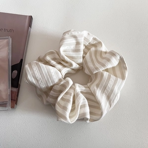 Detail shot of a cream striped fabric scrunchie with soft pleated texture and soft lighting