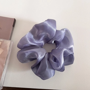 Close-up of light purple oversized scrunchie with glossy fabric on white textured surface
