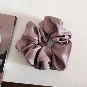Macro view of smoky pink satin scrunchie showing glossy pleated texture and elegant fabric