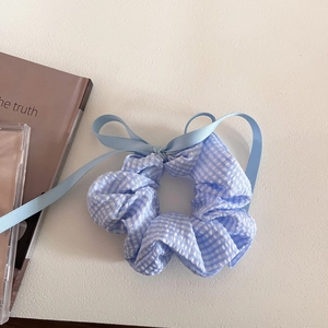 Detail of blue plaid scrunchie with a ribbon bow on a minimalist white desk