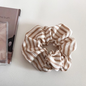 Detail of a large scrunchie with brown and white stripes on a minimalist textured background