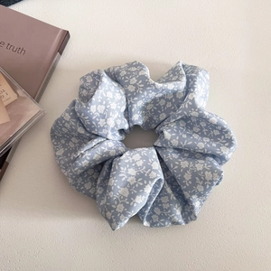 Close-up of light blue floral scrunchie with small white flowers on a textured surface