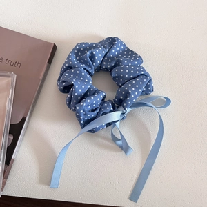 Detail view of blue polka dot hair scrunchie with ribbons on a textured surface