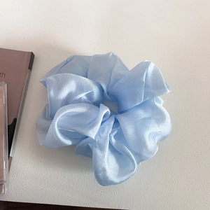 Detail of light blue pearlescent organza scrunchie with soft ruffled texture on white backdrop
