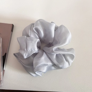 Detail of silver-grey satin scrunchie with glossy silk texture and elegant folds on a table