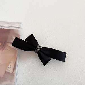 Detail of black satin bow hair clip with sparkling rhinestone center on white texture
