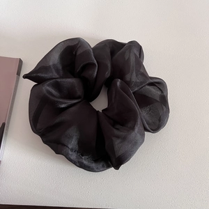 Detail of a large black organza scrunchie with soft silk luster on a white background