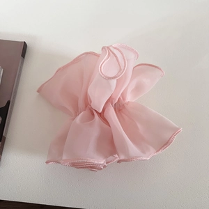 Detail of light pink layered organza scrunchie with soft pleats on a white surface
