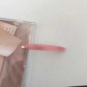Detail of pink acetate hair clip with golden lettering Barrette La France on white background