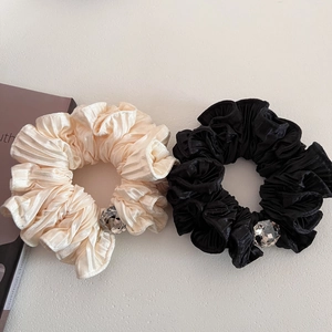 Close-up of pleated satin scrunchies with large crystal rhinestones in cream and black
