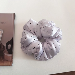 Close-up of a padded light purple satin scrunchie with black polka dots on white background