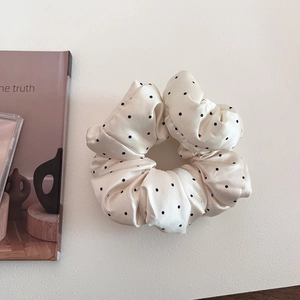 Detailed shot of white satin polka dot scrunchie with rich pleats on a minimalist surface