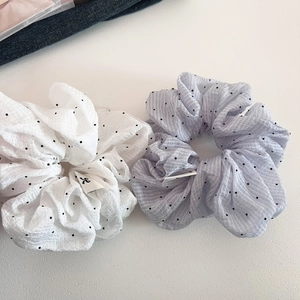 Detail of white and blue polka dot scrunchies with pleated fabric texture and logo tag