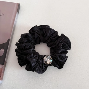 Elegant black pleated satin scrunchie with large crystal accent on gray surface