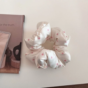 Detailed close-up of a large satin scrunchie with pink polka dots and soft pleated texture