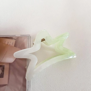 Detail of star-shaped hair claw clip in light green pearlescent resin with gold spring