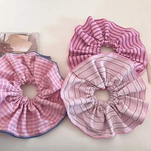 Trois grands chouchous roses à carreaux et rayures posés sur un magazine minimaliste